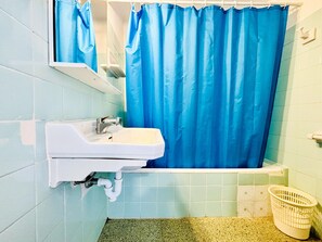 Une salle de bain avec un lavabo blanc, un rideau de douche bleu et un petit panier.
