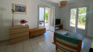 Una habitación con un banco de madera, un televisor sobre un soporte, un florero con flores y un cuadro en la pared.
