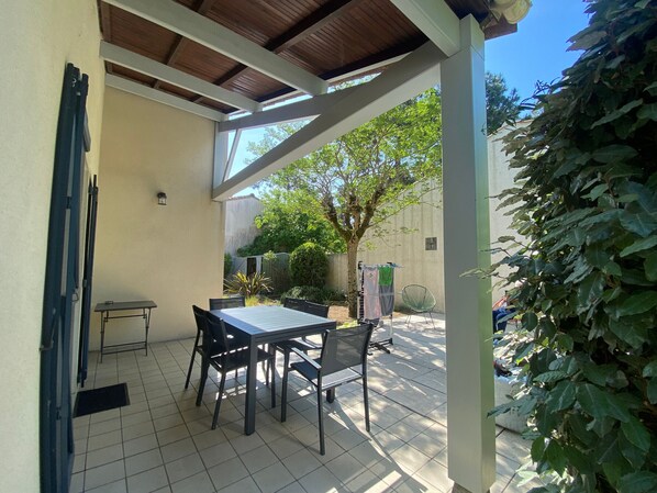 A covered patio area with a table and chairs, a small table, a clothesline, and a chair.