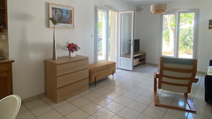 Un salón con un sofá, una silla de madera, un mueble para televisión, un jarrón con flores y un cuadro en la pared.