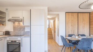 Una cocina moderna con armarios blancos, horno empotrado y comedor con mesa de madera y sillas grises.