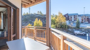 Un balcón con baranda de madera, una mesa y vista a un estacionamiento y edificios al fondo.
