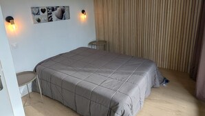 Makuuhuoneessa on sänky, kaksi seinään kiinnitettyä valaisinta, pieni pöytä ja ikkuna, jossa on sälekaihtimet.