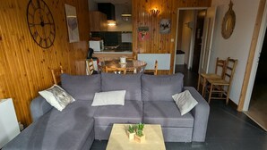 Moderni olohuone, jossa on harmaa kulmasohva, pieni puinen sohvapöytä ja taustalla ruokailutila.