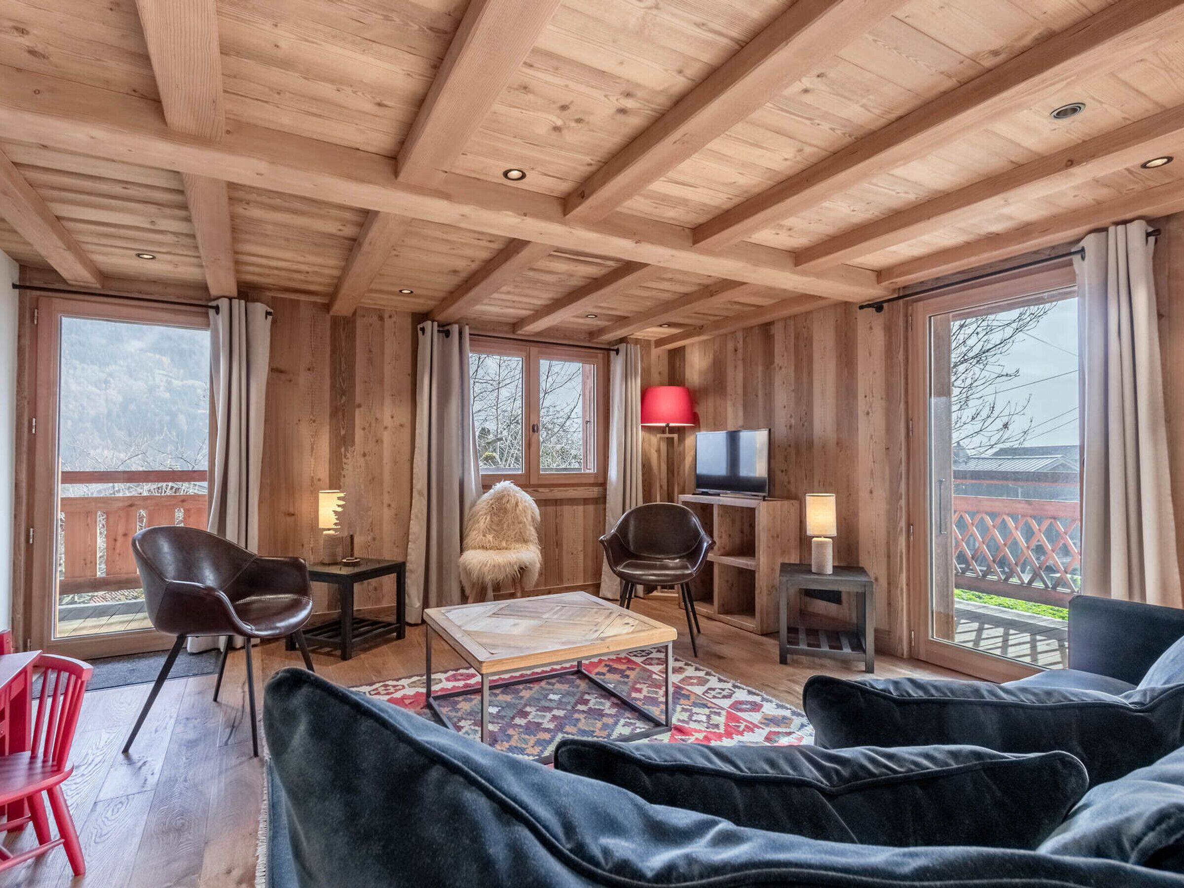 A cozy room with wooden beams, a TV, a fluffy chair, and a sofa.