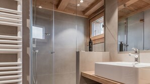 A modern bathroom with a glass shower enclosure, a large mirror, and a wooden vanity with a sink.
