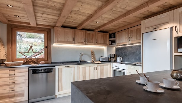 A modern kitchen with wooden cabinets, a dishwasher, a refrigerator, and a large island with cups and spoons.