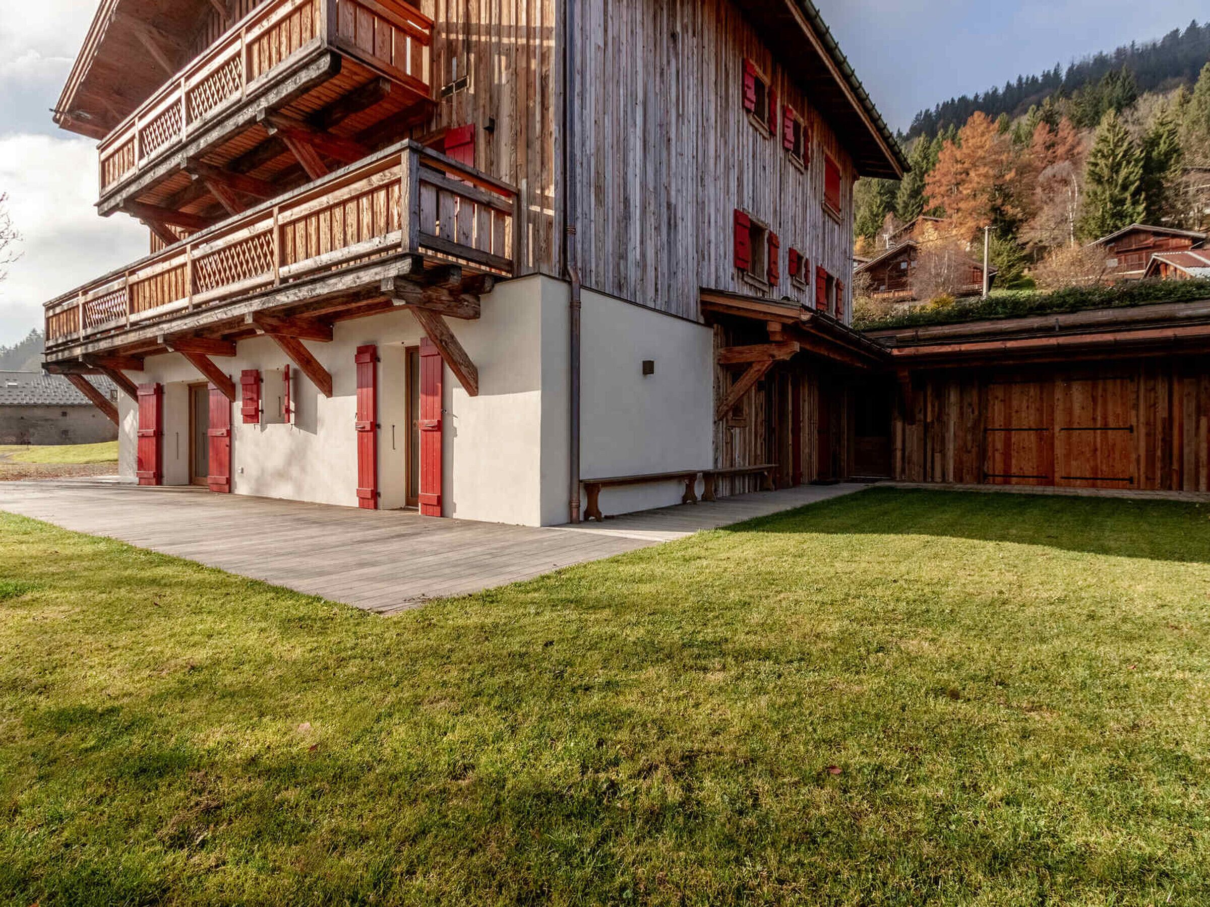 A two-story wooden building with balconies and red shutters, surrounded by a well-maintained lawn and a hilly backdrop.