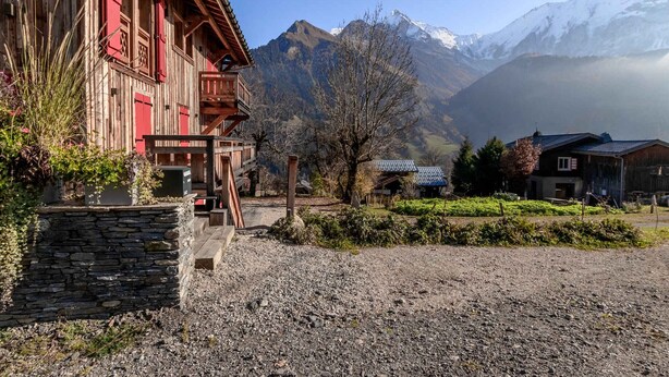 Un bâtiment rustique en bois, doté de fondations en pierre, d’un balcon et offrant une vue sur des montagnes enneigées en arrière-plan.