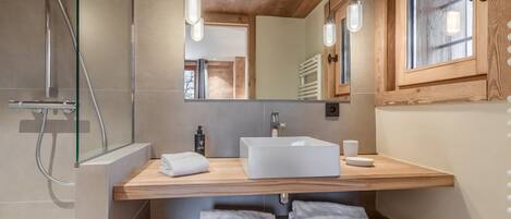 Un baño moderno con tocador de madera, un espejo grande y una ducha.