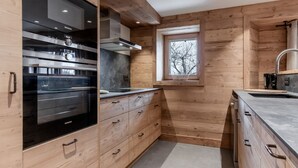 Une cuisine moderne avec des meubles en bois, un four encastré et une fenêtre donnant sur les arbres.