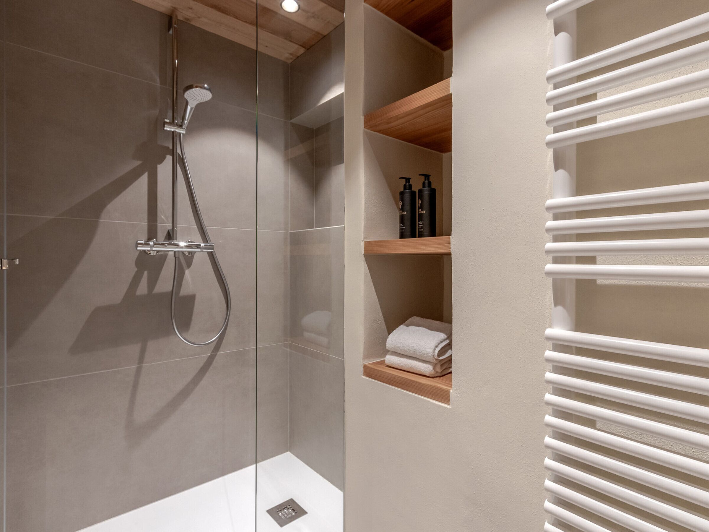 Un baño moderno con ducha de vidrio, repisas de madera y un toallero blanco.