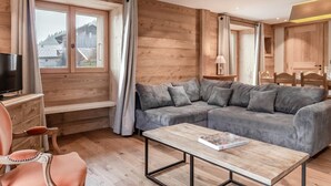 Une pièce chaleureuse avec un décor intérieur en bois, un canapé d’angle, un téléviseur et une table avec un livre.