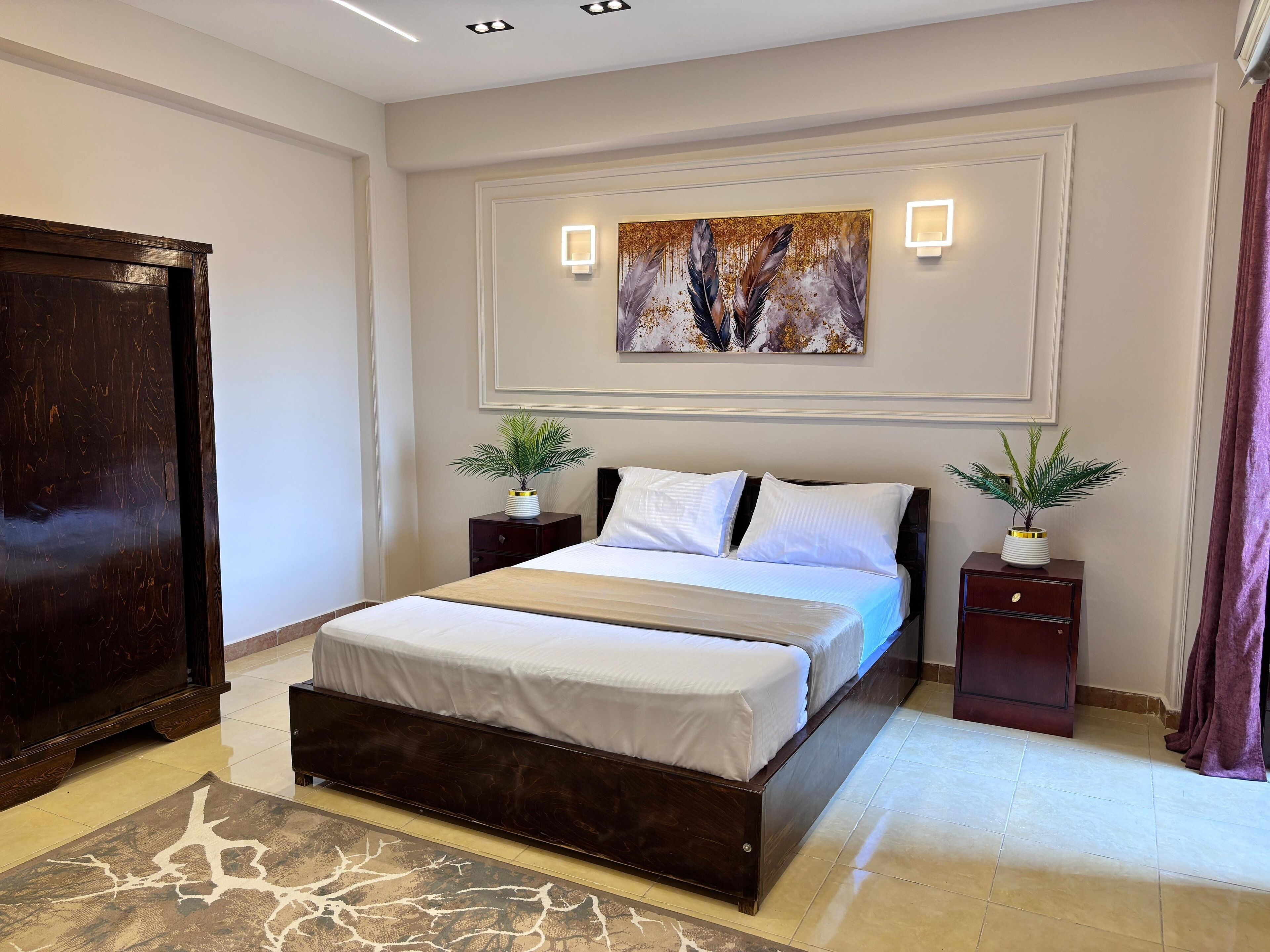 Ein modernes Schlafzimmer mit einem großen Bett, zwei Nachttischen mit Pflanzen, einem dunklen Holzschrank und einem dekorativen Gemälde über dem Bett.