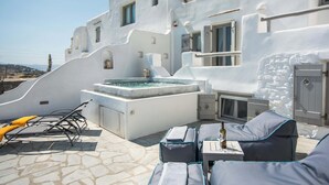 Una terraza en la azotea con jacuzzi, sillones de descanso y suelo de piedra.
