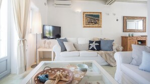 Una sala de estar con un sofá blanco, un televisor, un cuadro y un aparador de madera.