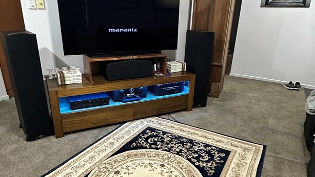 Un salon avec un téléviseur à écran plat posé sur un meuble en bois, un tapis à motifs et un buffet en bois.