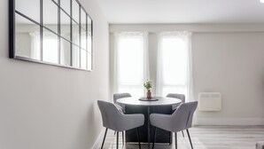 Een moderne eethoek met een ronde tafel, vier grijze stoelen en een potplant.