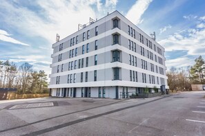 Ein modernes, mehrgeschossiges Gebäude mit flachem Dach, großen Fenstern und einem Parkplatz davor.