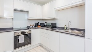 Een moderne keuken met witte kastjes, een ingebouwde oven, een magnetron en een roestvrijstalen spoelbak.