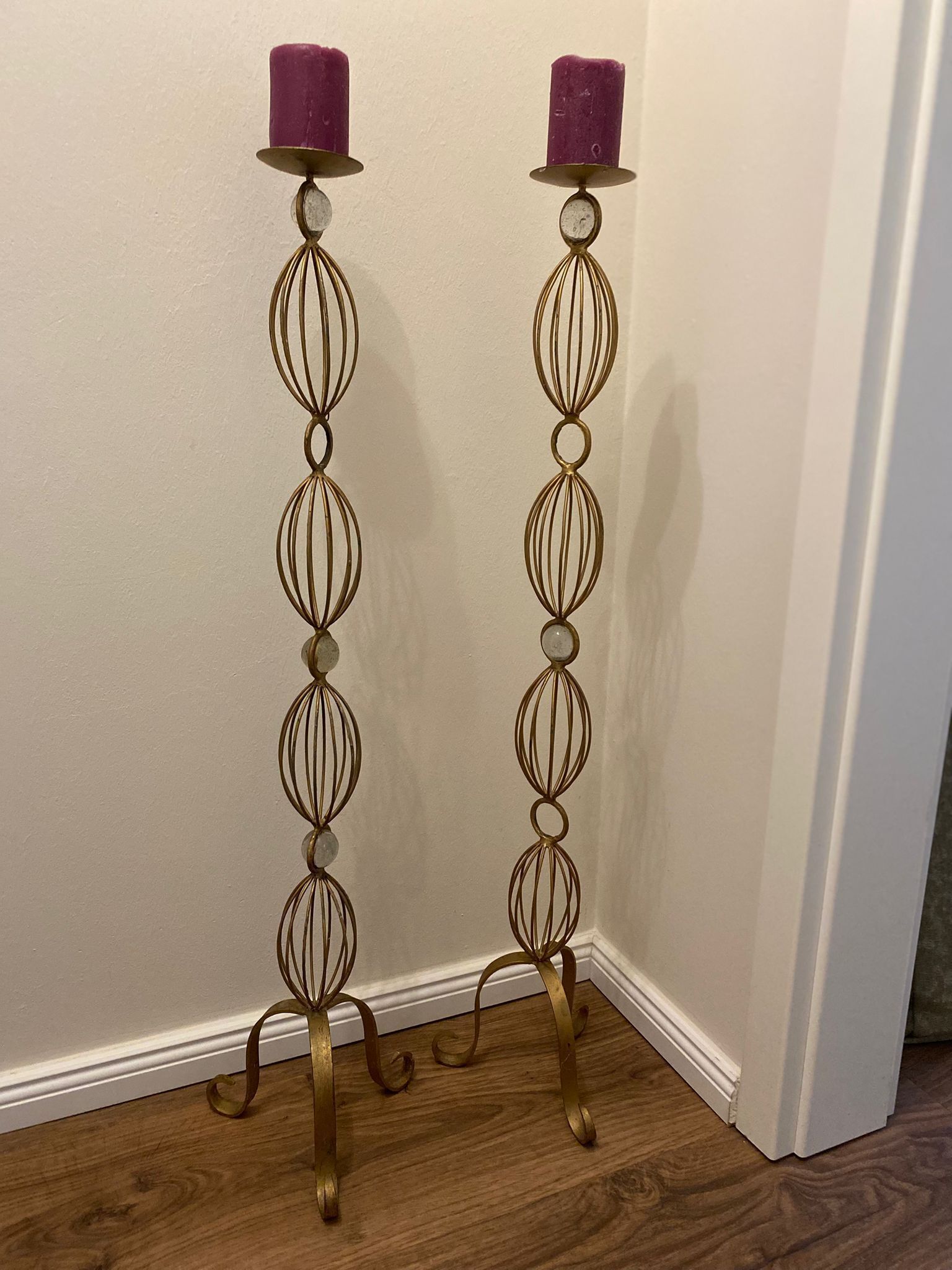 Suporte de velas metálico alto e ornamentado, com base circular e design em espiral, posicionado contra uma parede lisa.