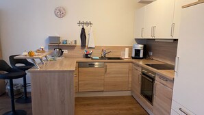 Eine kompakte Küche mit Holzausstattung, einer Kaffeemaschine, einem Geschirrspüler und einer kleinen Essecke mit zwei Stühlen.