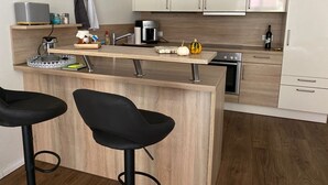 Eine moderne Küche mit einer zentralen Kochinsel, zwei schwarzen Barhocker, einer Kaffeemaschine und einer Weinflasche.