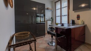 Uma cozinha compacta com armários escuros, forno embutido, pequena área de refeições com um banco de bar e uma janela com persianas.