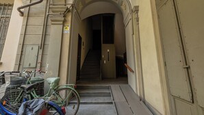 Um corredor estreito com uma escada que leva a uma porta. Bicicletas estão estacionadas no lado esquerdo.