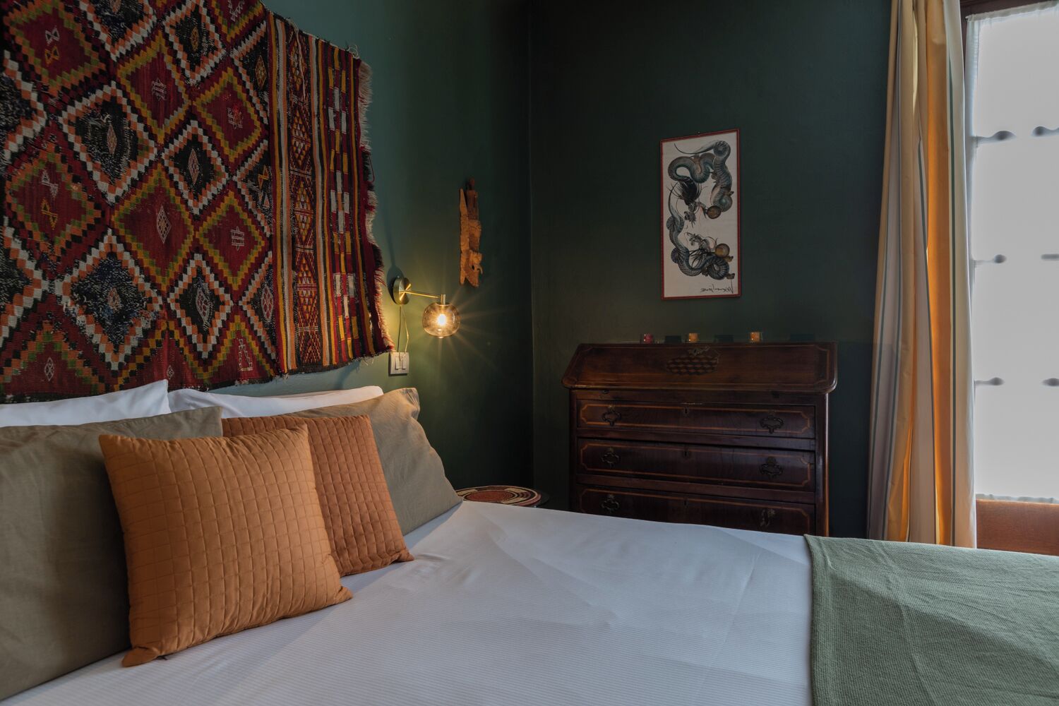 A bedroom with a bed, pillows, a wall hanging, a dresser, and a framed picture.