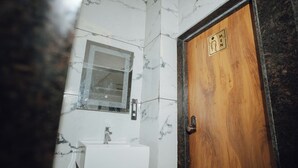 Un baño con pared de mármol, puerta de madera y lavamanos blanco.