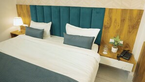 Una habitación de hotel con cama, mesita de noche, lámpara, teléfono y una planta en maceta.
