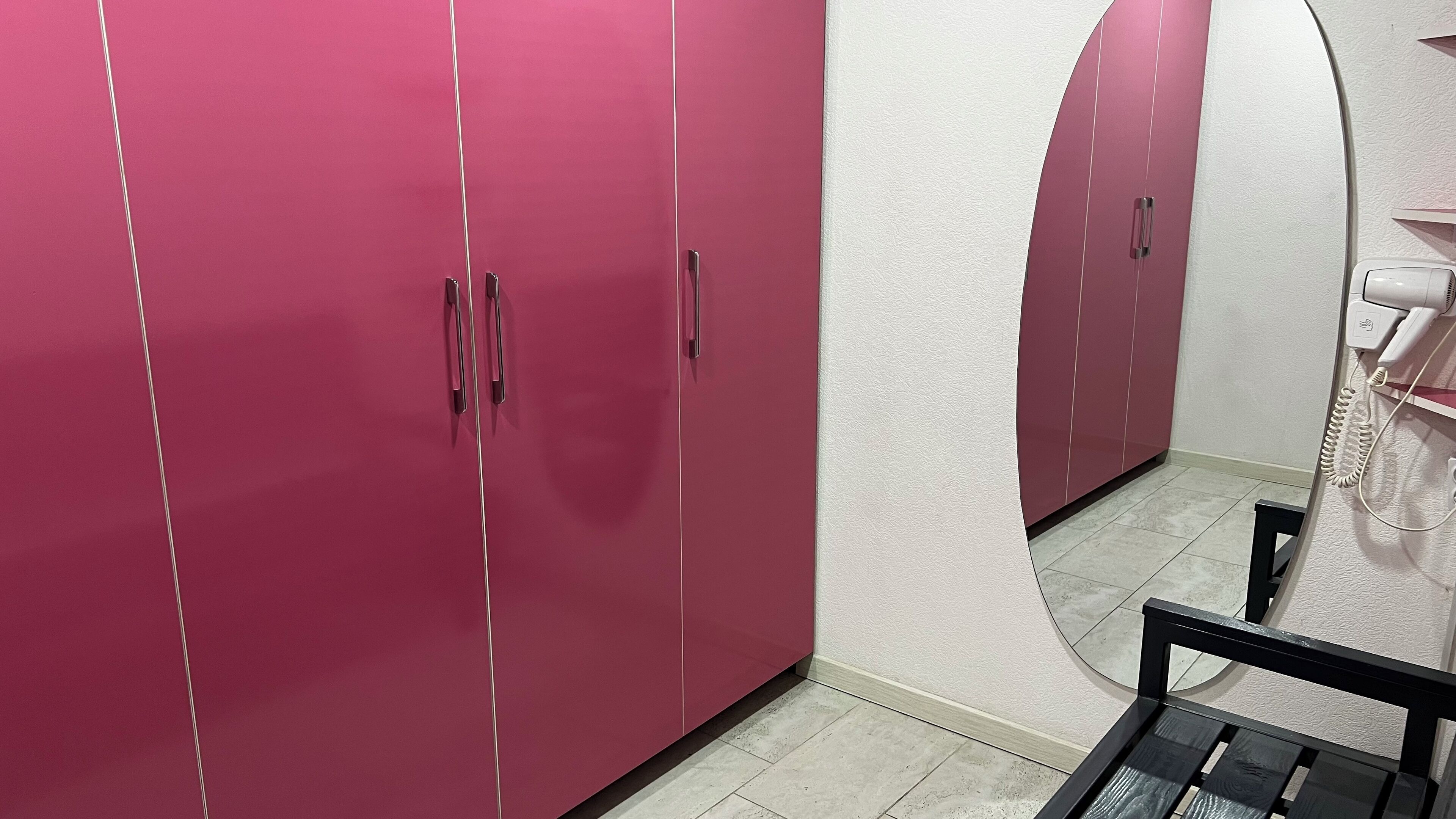 A room with pink cabinets, a white wall, and a mirror reflecting the cabinets.