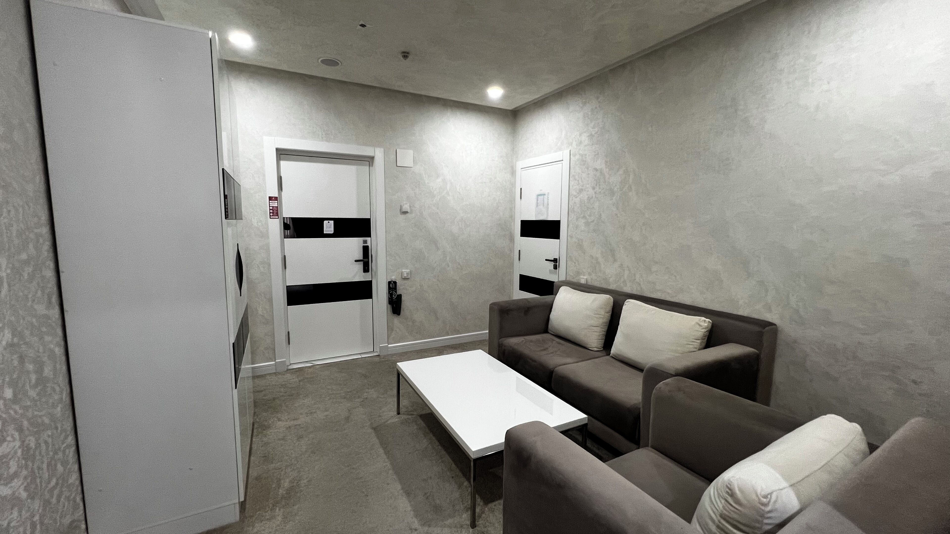 Una habitación moderna y minimalista con sofá, una mesita de centro y una puerta con teclado de seguridad.