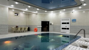 A hotel pool area with a clear pool, lounge chairs, a table with drinks, and a door with a sign. - Ohu Palace Hotel (Fergana)
