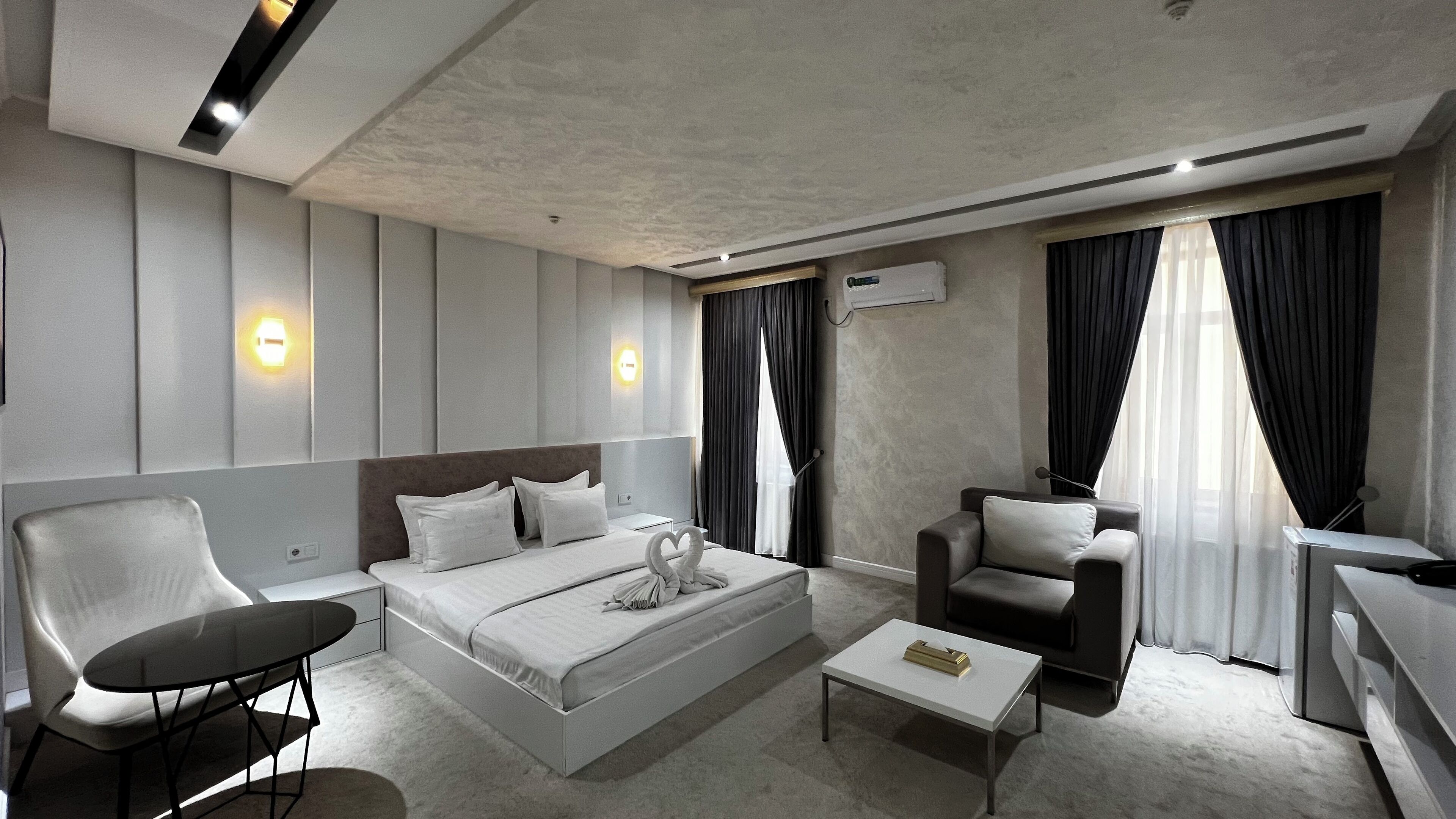 Een moderne hotelkamer met een groot bed, twee fauteuils, een klein tafeltje en een bureau.