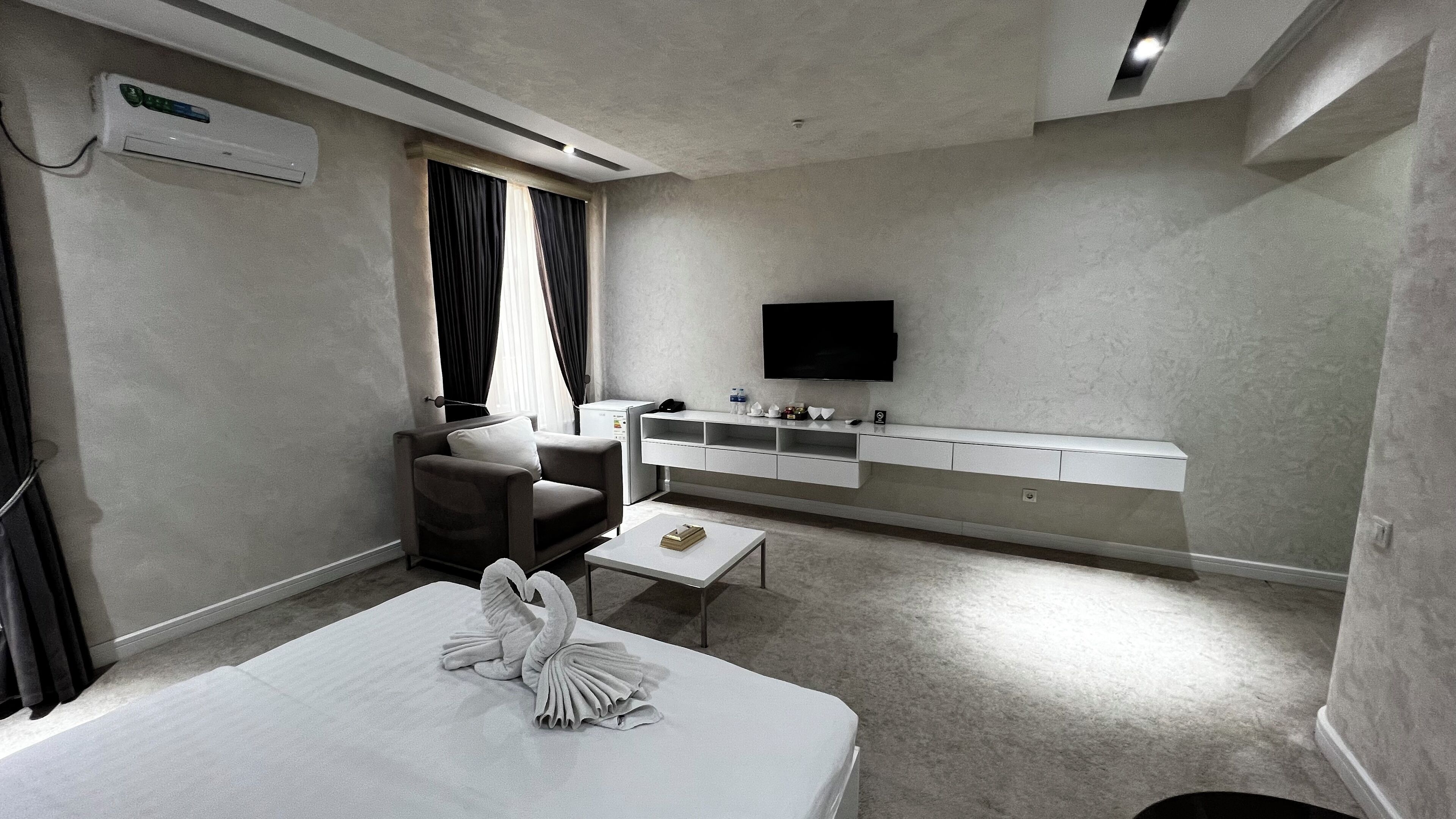 Une chambre d’hôtel équipée d’un lit, d’un canapé, d’une télévision, d’un minibar et d’une fenêtre avec des rideaux.