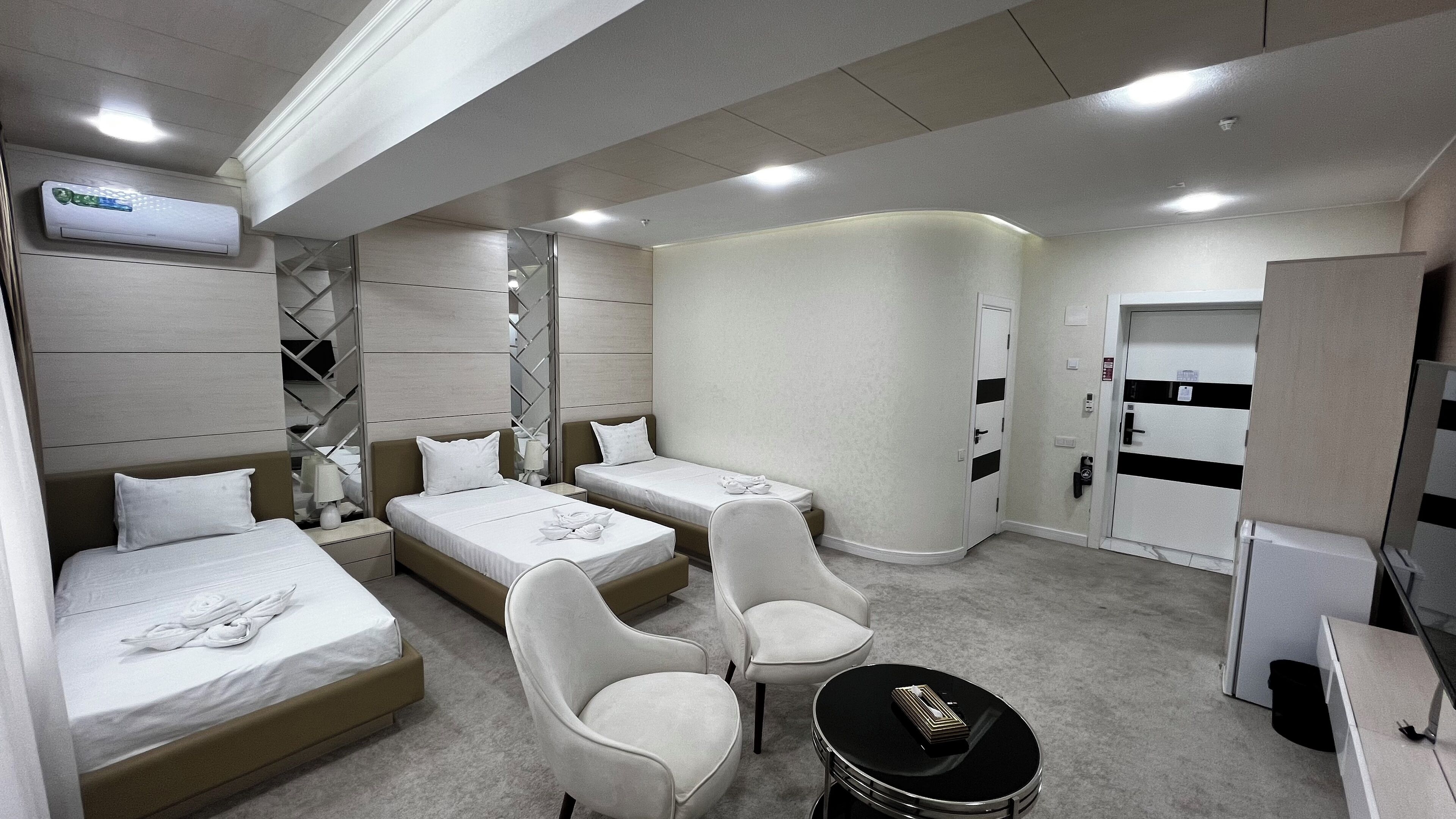 A hotel room with two single beds, a sofa bed, two armchairs, a small table, and a minibar.