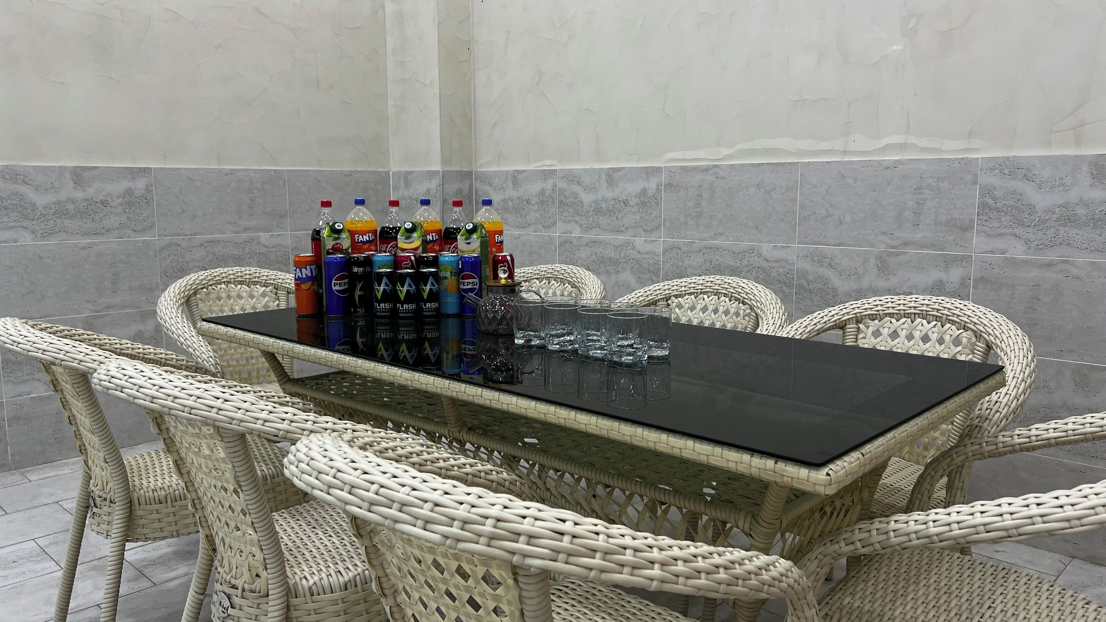 A table with a black surface surrounded by wicker chairs, and various soda cans and glasses on the table.