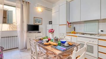 A modern kitchen with white cabinetry, a dining table set for breakfast, and a television on a stand.