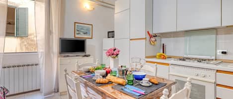 A modern kitchen with white cabinetry, a dining table set for breakfast, and a television on a stand.