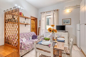 A cozy living room with a floral sofa, a dining table set for two, a television, and a kitchen area with a refrigerator. - Casa Lilly Sanremo La Pigna Old Town Hideaway (Sanremo)