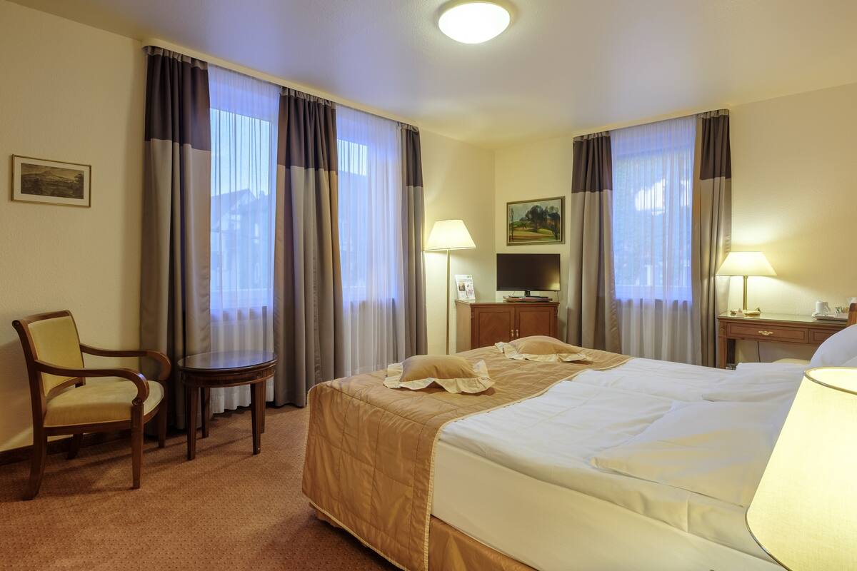 Une chambre d’hôtel avec un lit, une chaise, une table, une lampe et des rideaux.