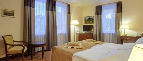 Una habitación de hotel con cama, una silla, una mesa, una lámpara y cortinas.