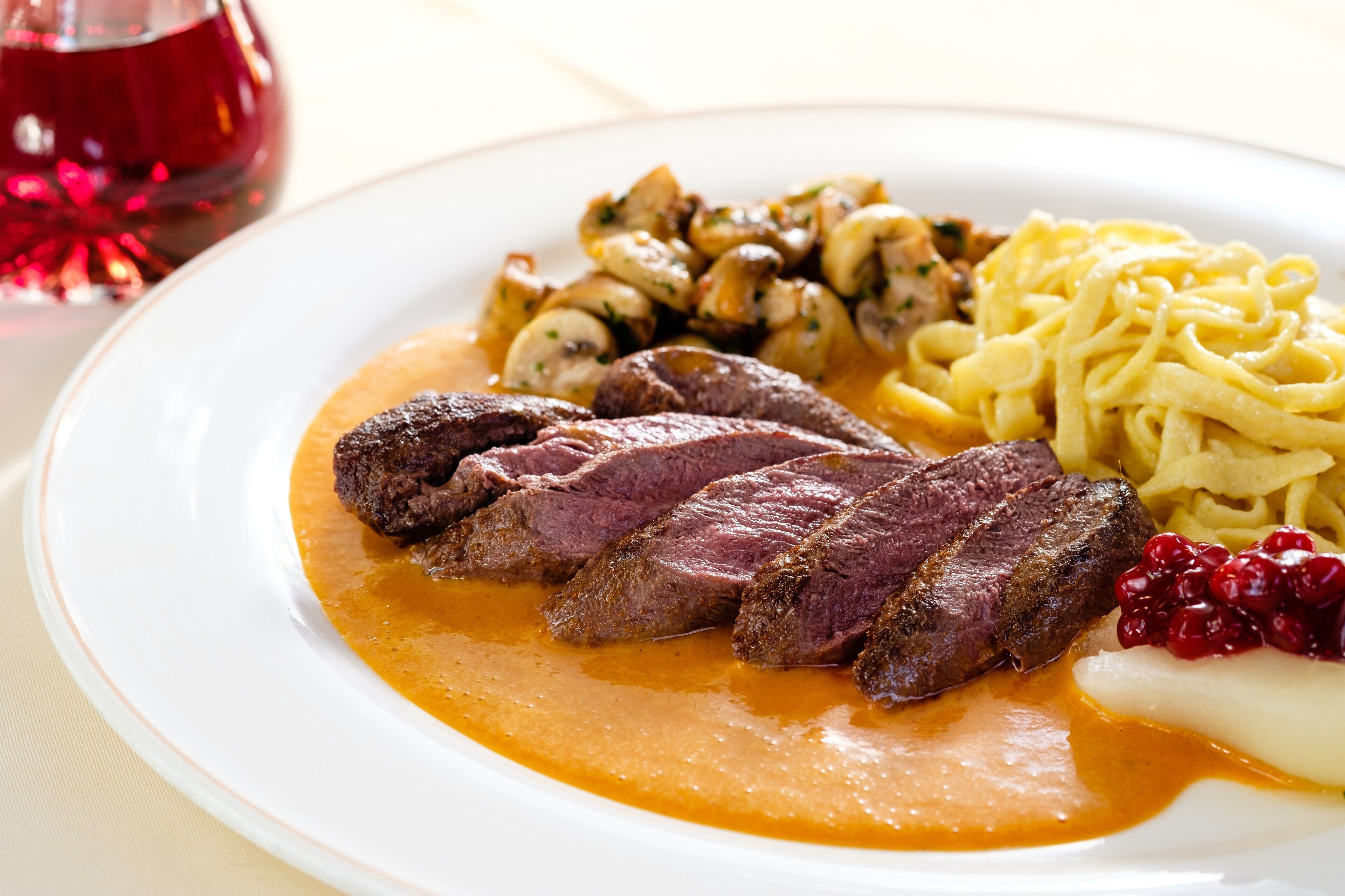 Un plato de comida que incluye carne, champiñones, fideos y arándanos.