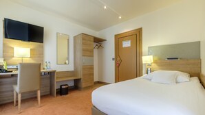 Habitación de hotel con cama, escritorio, silla, televisor y espejo.