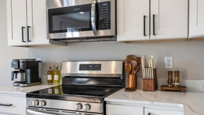 A modern kitchen with stainless steel appliances, including a microwave, oven, and stove. There are wooden utensils and a coffee maker on the counter.
