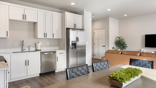 A modern kitchen with white cabinets, a stainless steel refrigerator, and a dining area with a table and chairs.