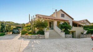 Ein Haus im mediterranen Stil mit einer Steinaußenwand, einem Ziegeldach und einer zentralen Treppe zum Eingang.