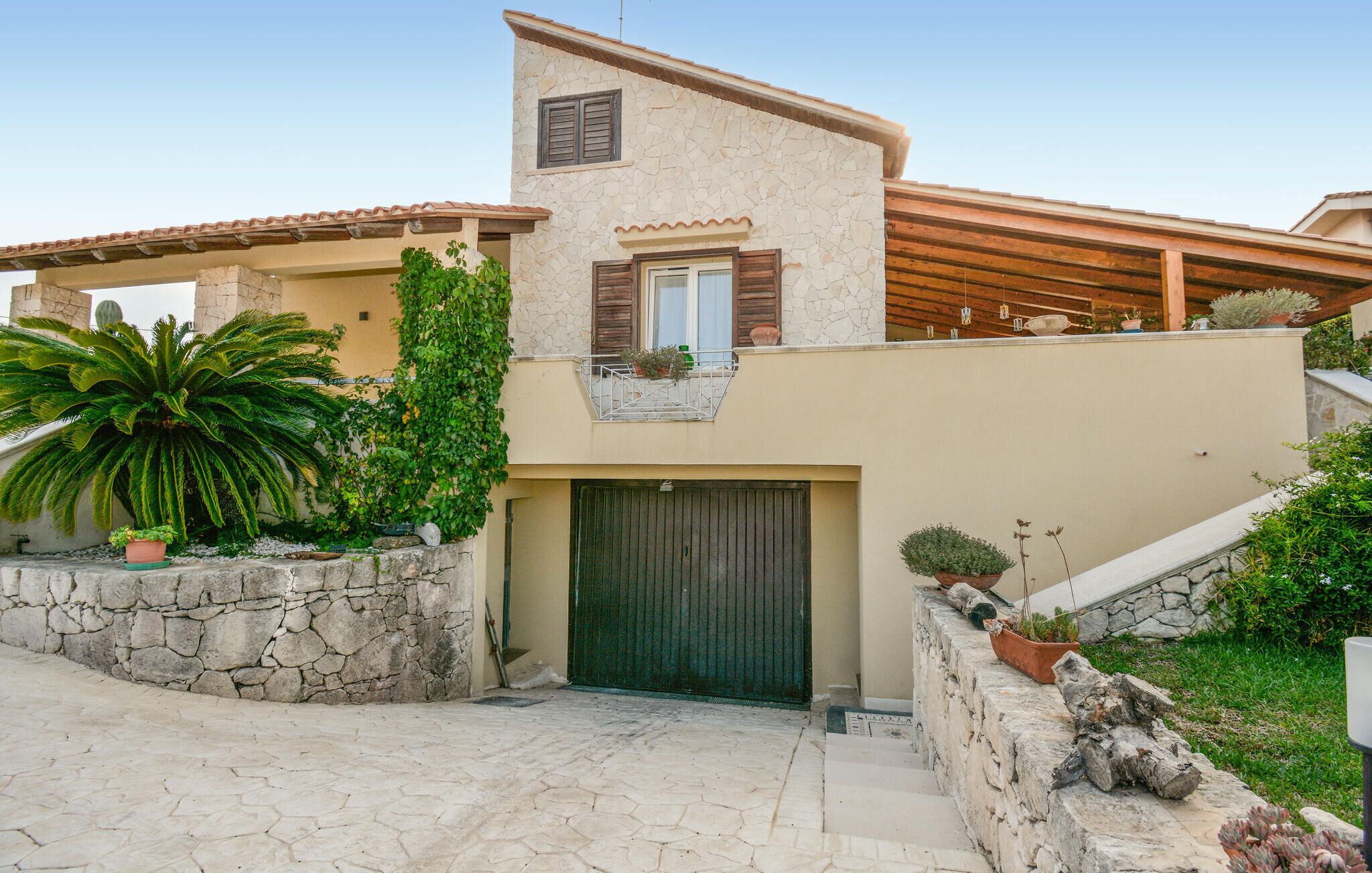 A two-story house with a stone facade, a green door, and a balcony with potted plants.